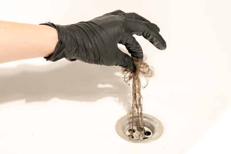 A gloved hand lifts hair and other obstructions from a shower drain