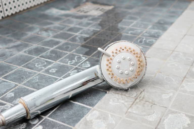 A shower head and floor which show major signs of hard water scaling.