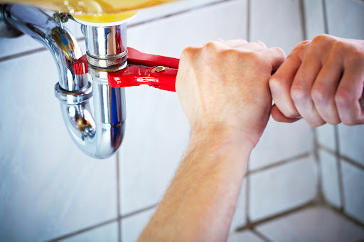 Plumber hands holding wrench and fixing a sink in bathroom.