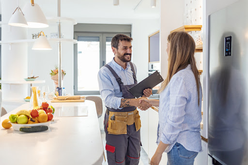Young Woman Shaking Hands To Male Plumber With Clipboard In Kitchen Room