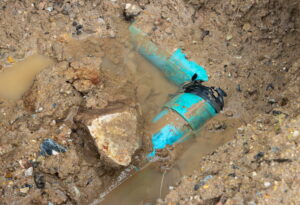 A blue plastic pipe in the ground which is broken and surrounded by water and mud.