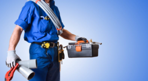 A plumber neck down carrying a toolbox, and is covered shoulders down in different plumbing tools.