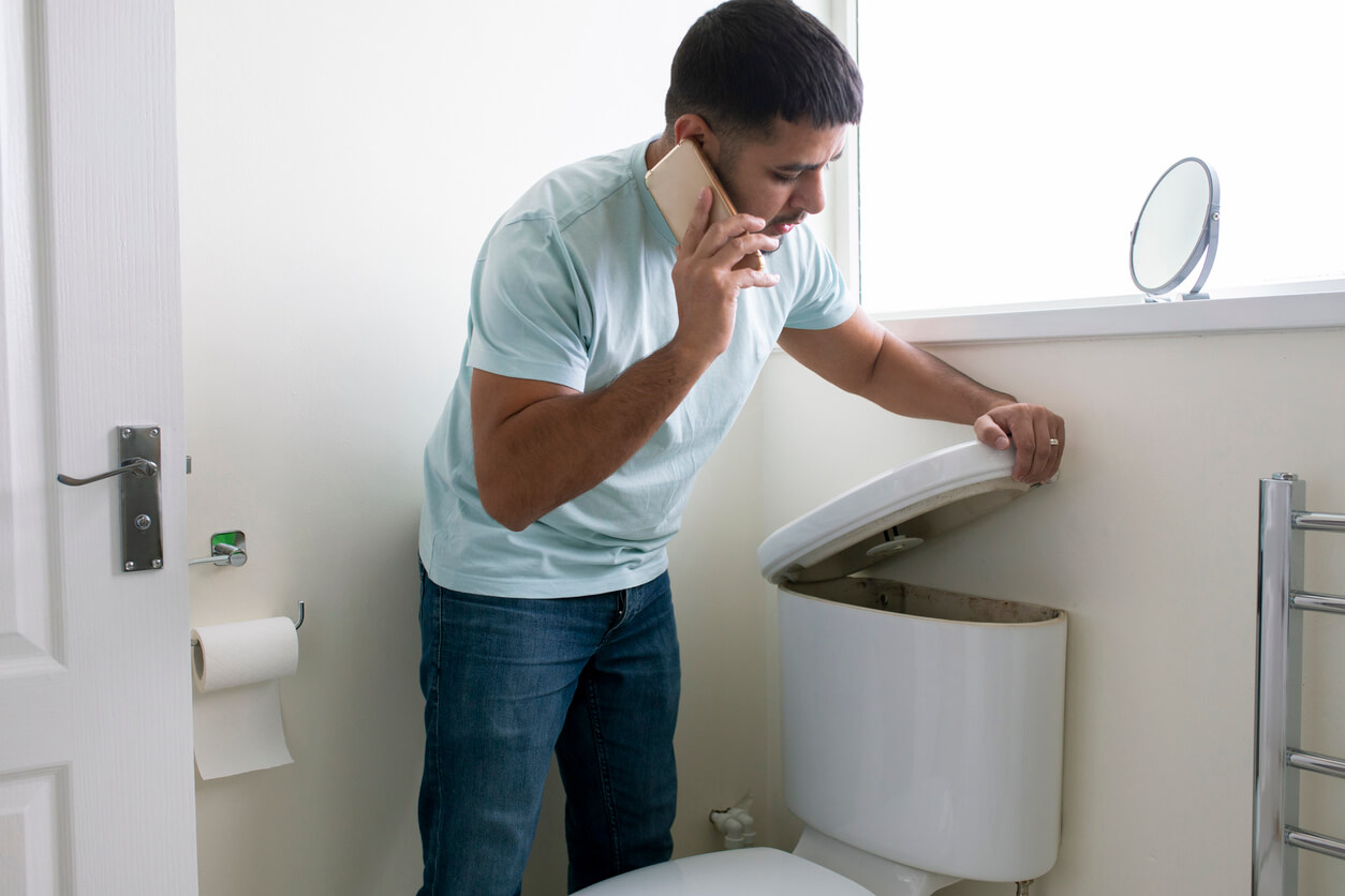 man looking at toilet and alling a plumber