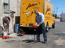 Plumber from Larkin Plumbing looking for leaks with leak detection tool near a commercial building.