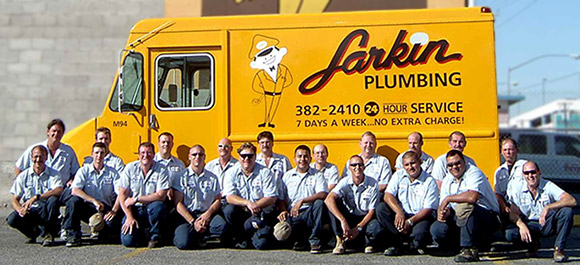 The Larkin Plumbing team sitting and kneeling in front of yellow Larking Plumbing work van