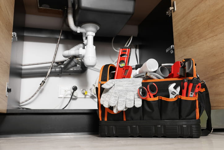 A plumber's tool bag on the floor underneath a kitchen sink.